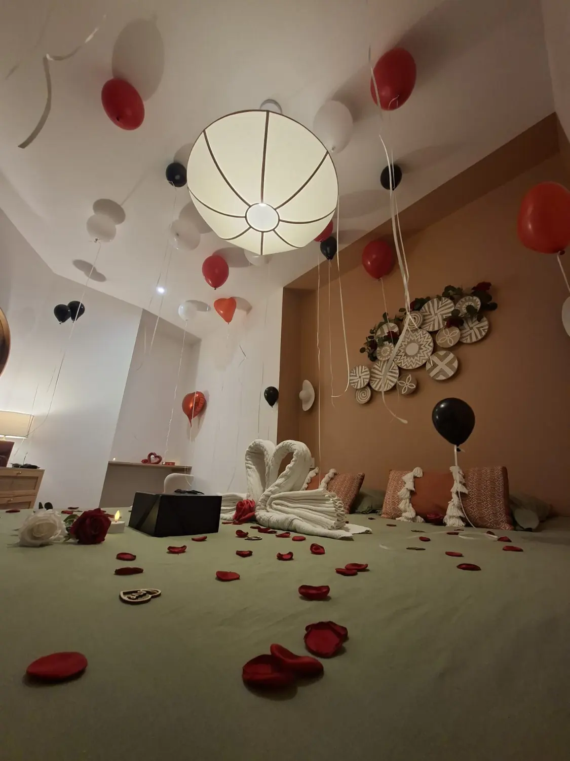 Vue d'ensemble de la chambre romantique aux murs terracotta, ballons et pétales