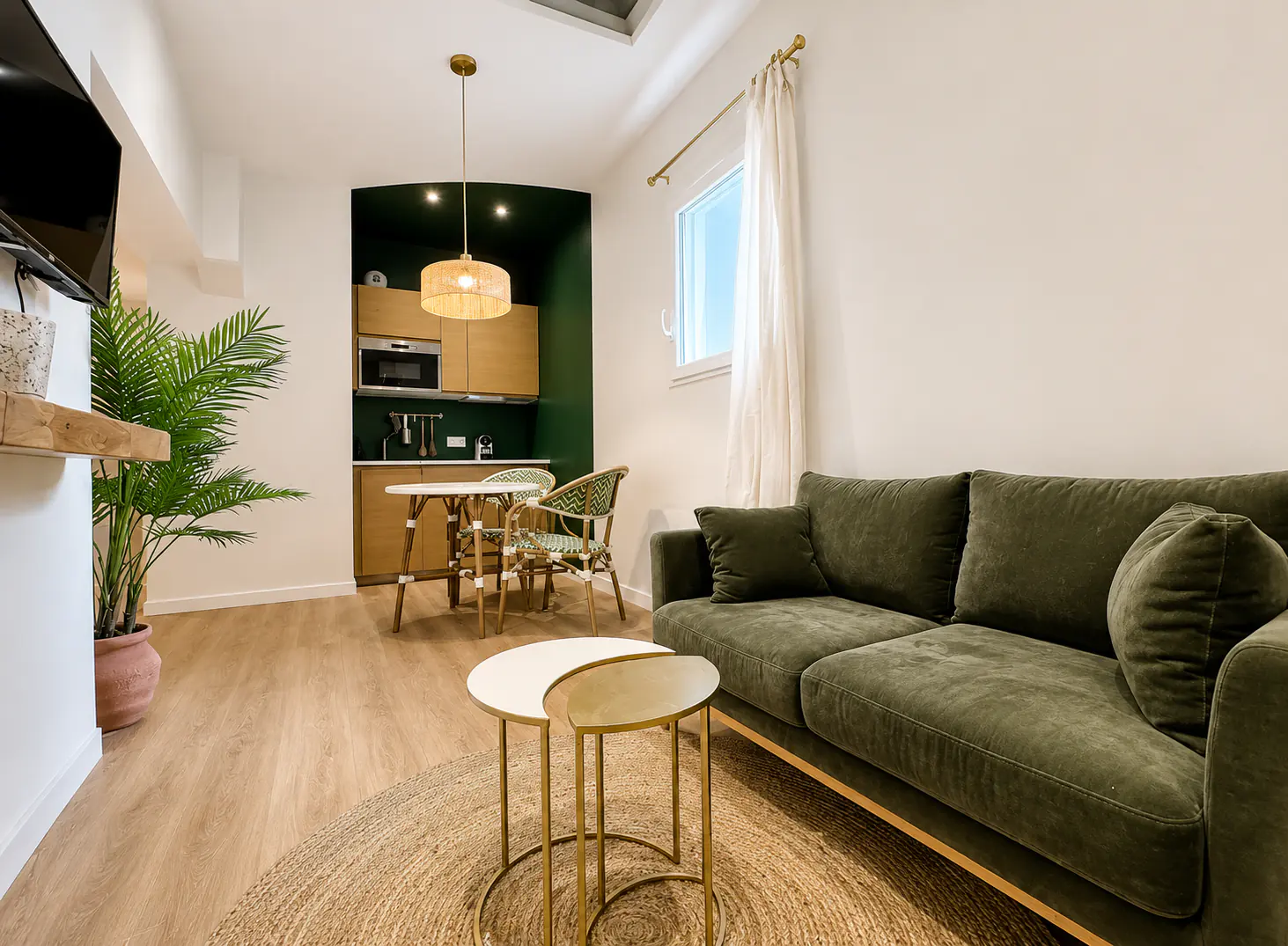 Salon cosy avec canapé en velours vert, tables gigognes dorées et puits de lumière