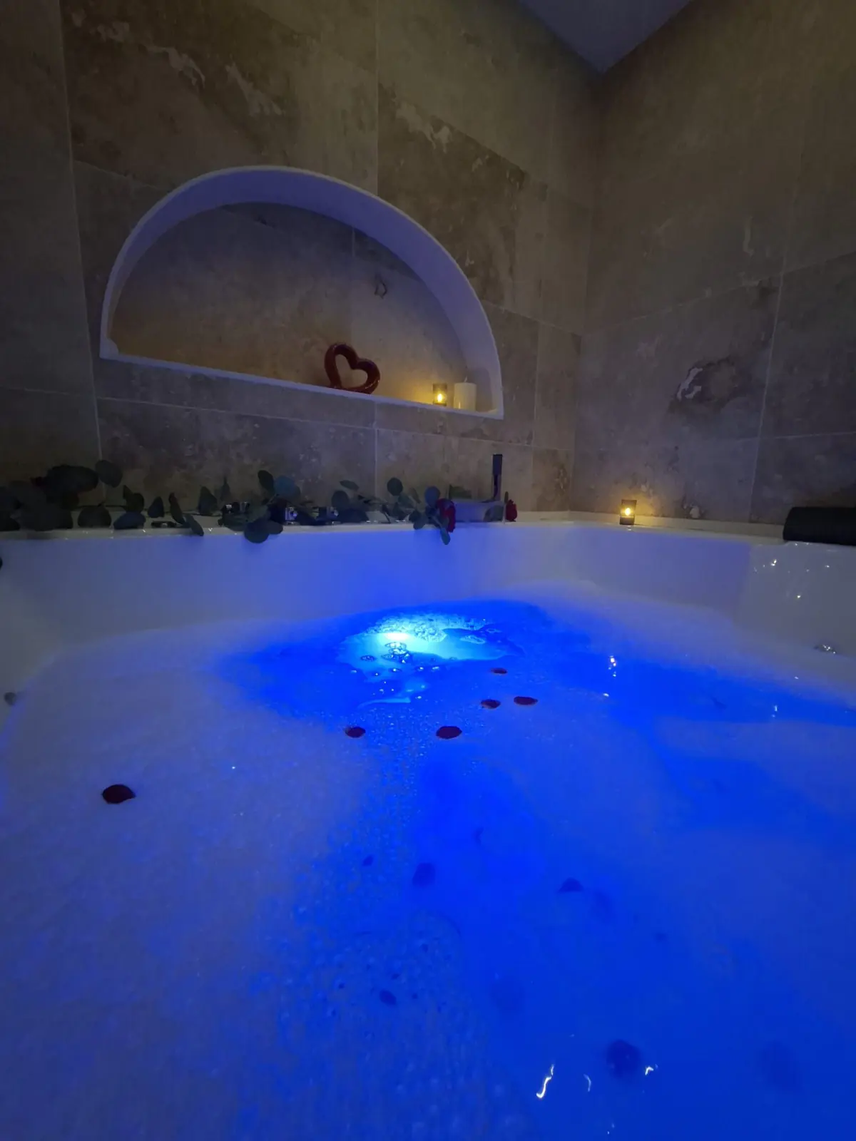 Bain à remous mousseux la nuit, cœur rouge et bougies dans la niche de pierre